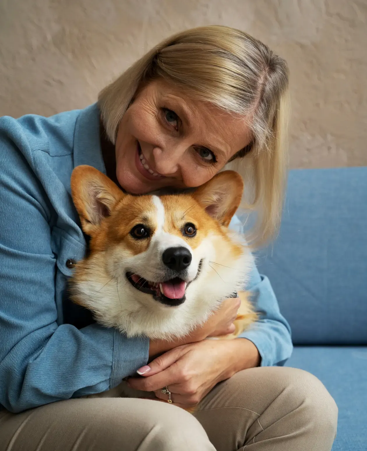 Woman hugging her corgi on the sofa